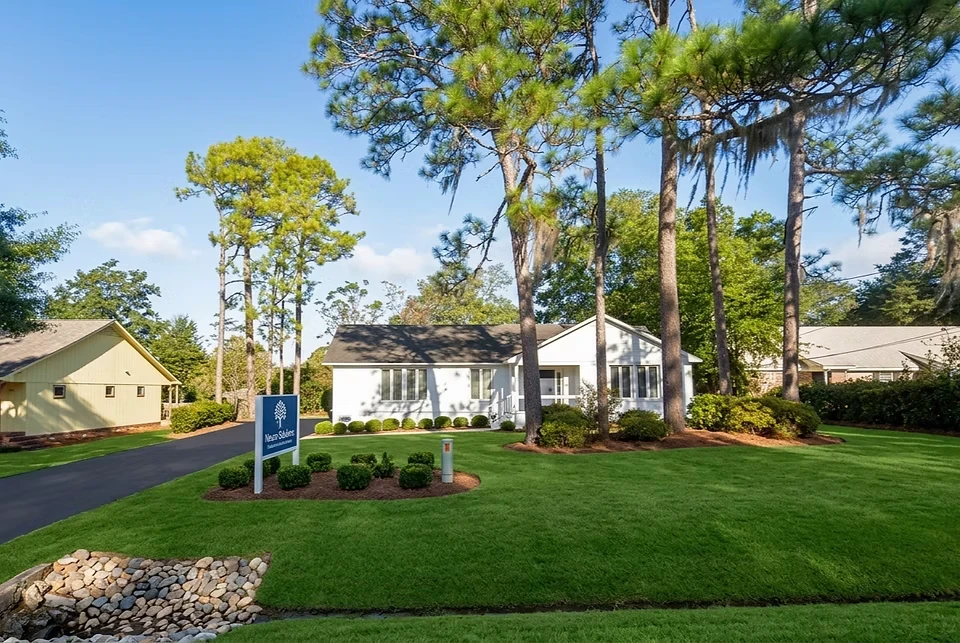 Charming office nestled among tall pine trees, featuring a manicured lawn and a welcoming atmosphere.